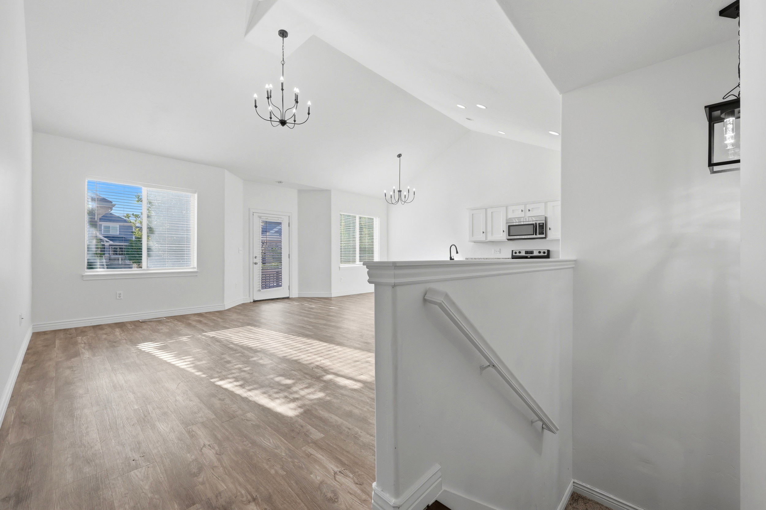 Open-concept living area featuring wood-finish flooring, vaulted ceilings, and a contemporary chandelier