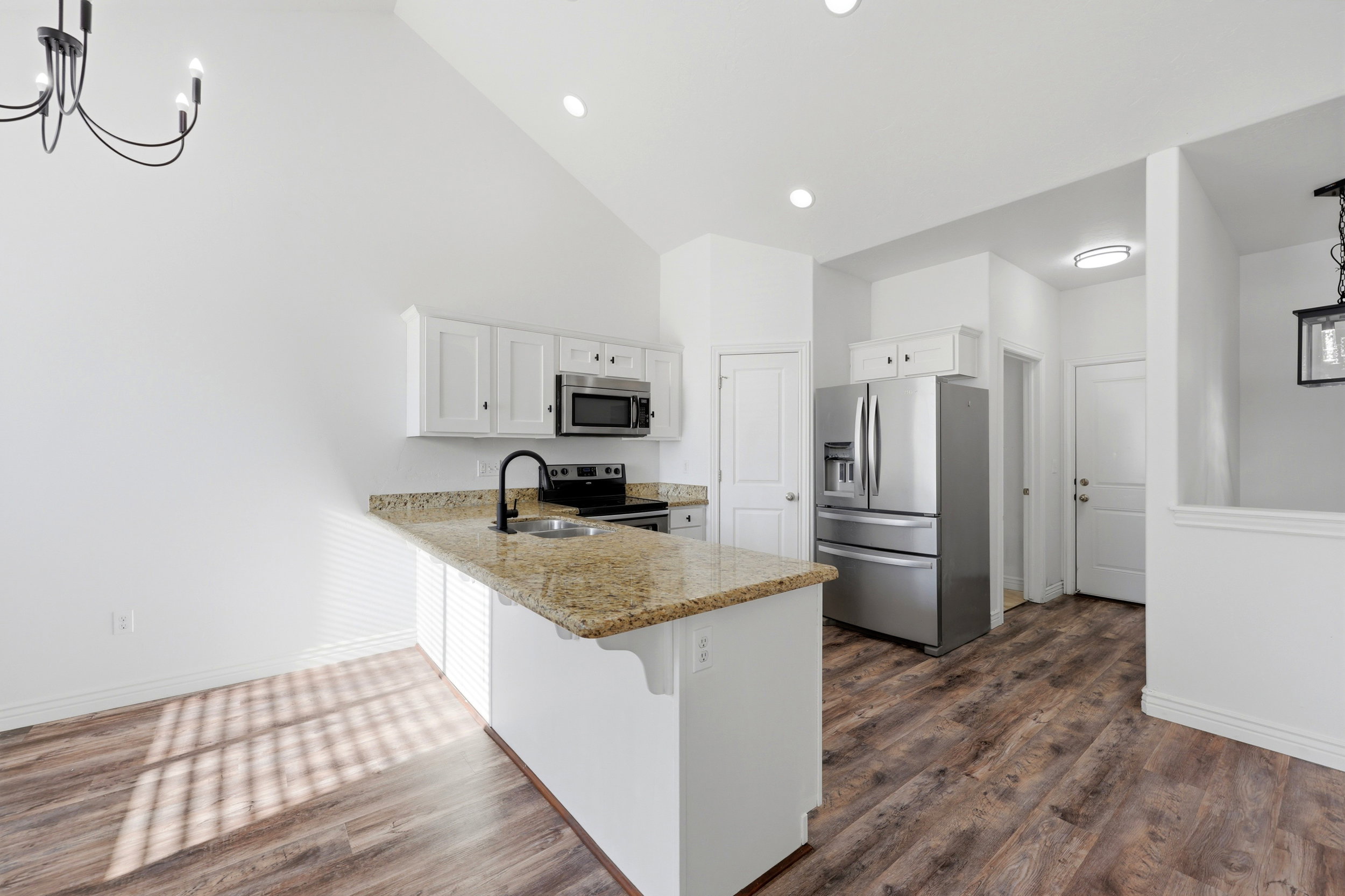 Open-concept kitchen featuring wood-finish flooring, a vaulted ceiling, recessed lighting, white cabinetry, and stainless steel appliances