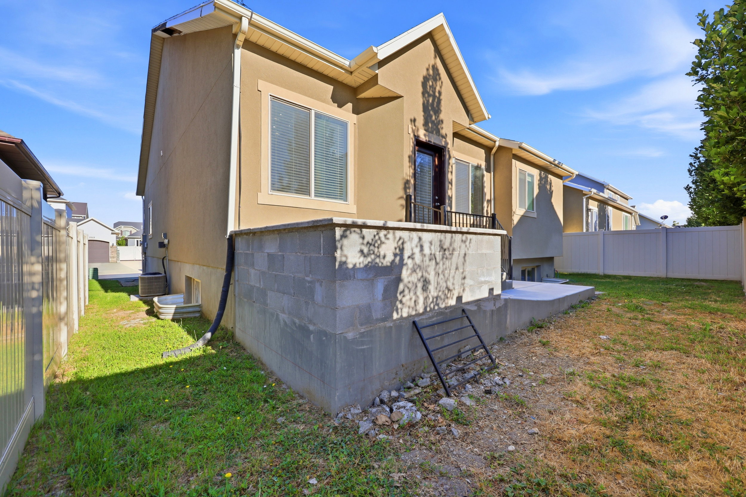 Rear exterior featuring stucco siding, white window trim, a black balcony railing, and a concrete patio