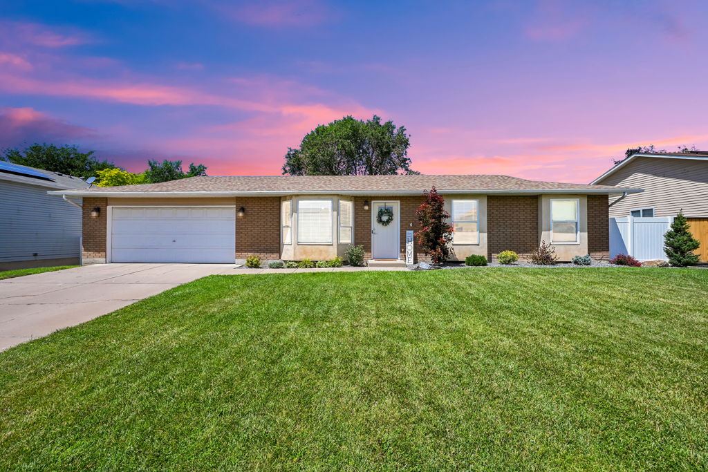 Mid-century modern brick rambler featuring an attached two-car garage, established landscaping, bay window, and a white entry door