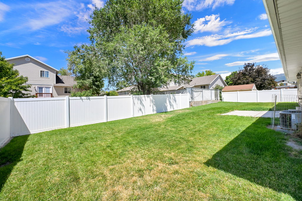 Expansive lawn area surrounded by white privacy fencing, featuring a concrete patio pad