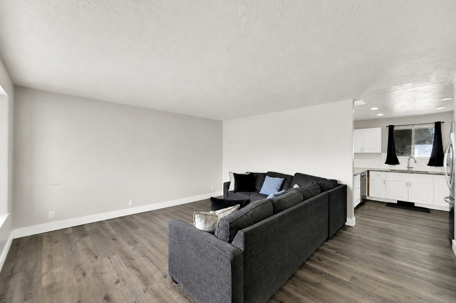 Spacious living area featuring wood-finish flooring, light-toned walls, and a large window