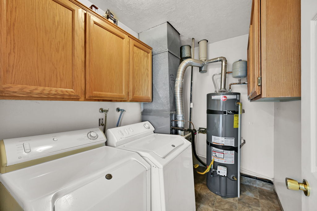 Utility space featuring wood-finish cabinetry, a hot water heater, and durable flooring