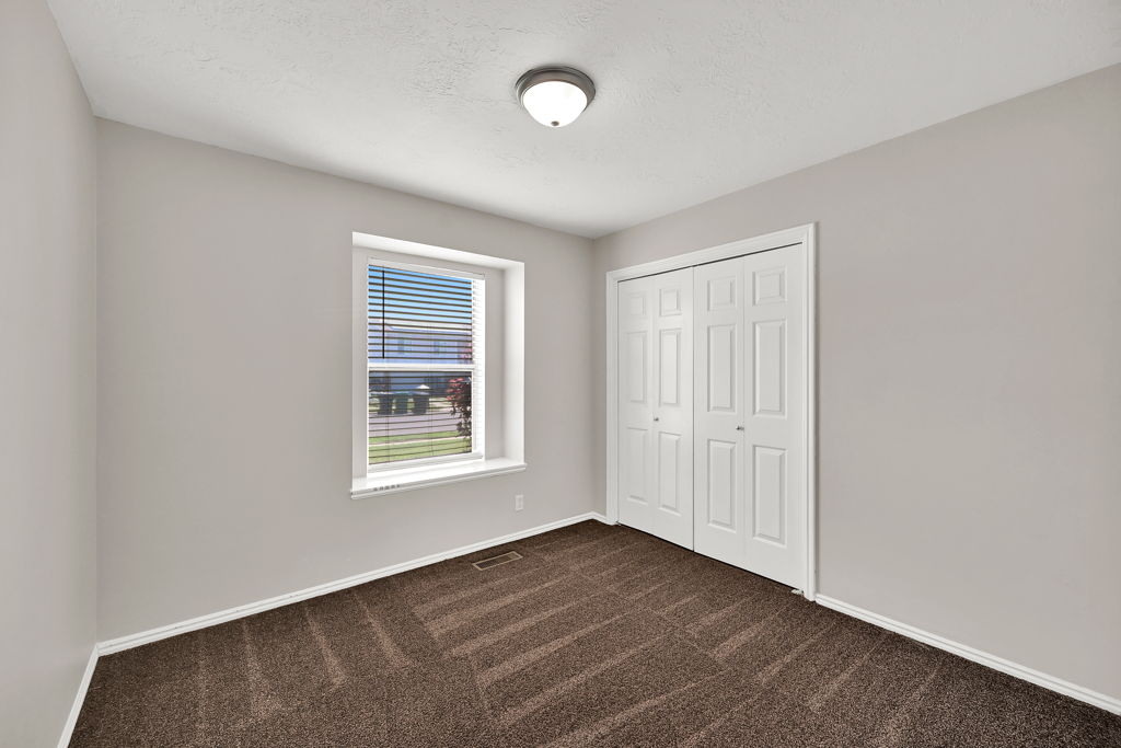 Interior room featuring neutral wall paint, brown patterned carpeting, and a white bi-fold closet