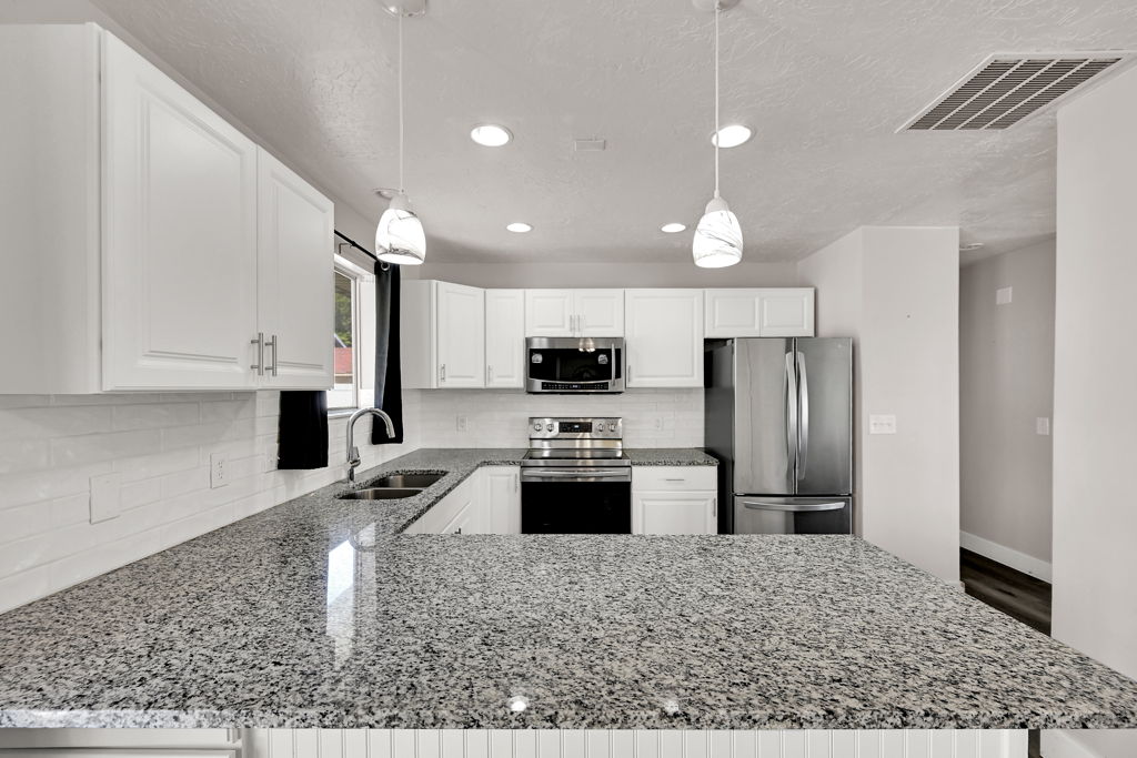 Kitchen featuring white cabinetry, speckled countertops, stainless steel appliances, and a subway tile backsplash