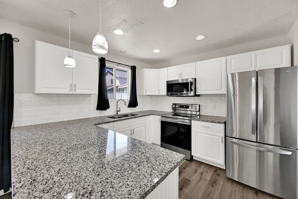 Kitchen featuring white shaker cabinetry, stainless steel appliances, speckled stone countertops, a subway tile backsplash, and wood-finish flooring