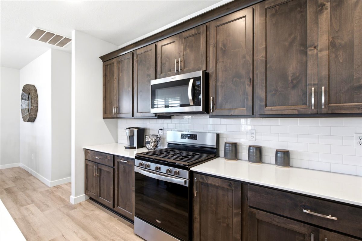 Kitchen featuring dark wood-finish cabinetry, stainless steel appliances, white subway tile backsplash, and light-toned countertops