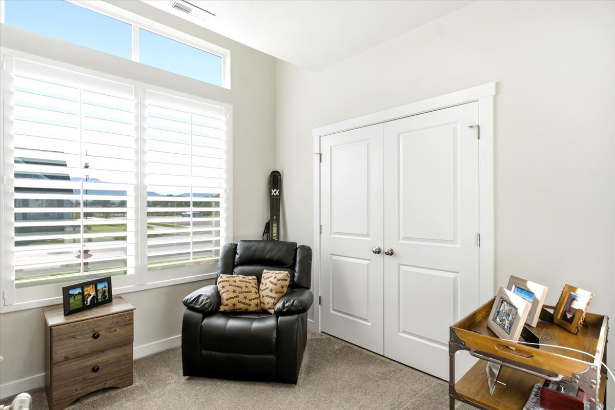 Room featuring tall windows with white plantation shutters, an upper transom window, light-toned carpeting, white walls, and a double bi-fold door