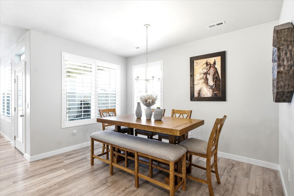 Dining area featuring wood-finish flooring, two large windows with plantation shutters, a contemporary chandelier, and light gray wall paint