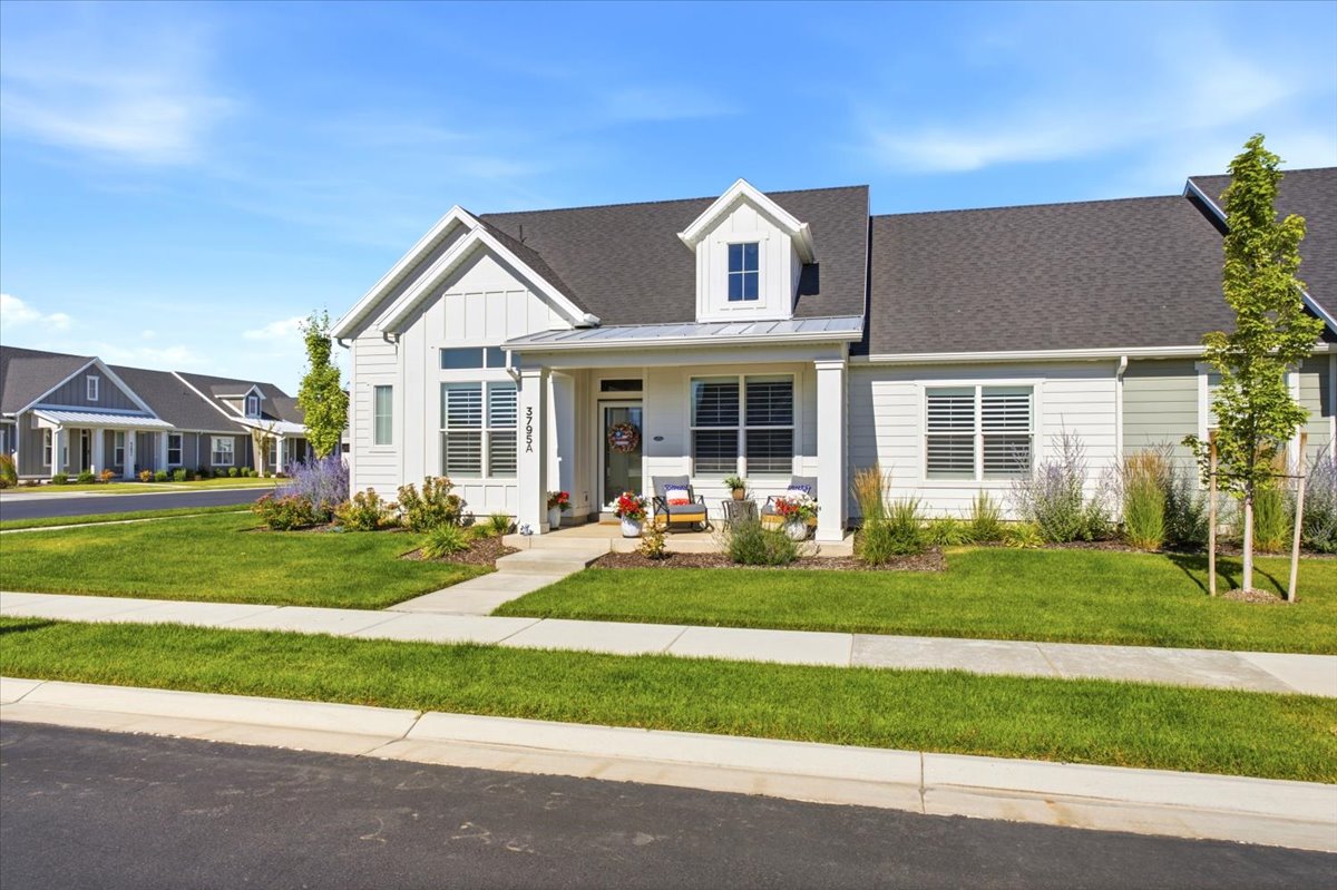 Contemporary exterior featuring light-colored siding with board and batten accents, a covered front porch, a dormer window, dark shingle roofing, and a concrete walkway