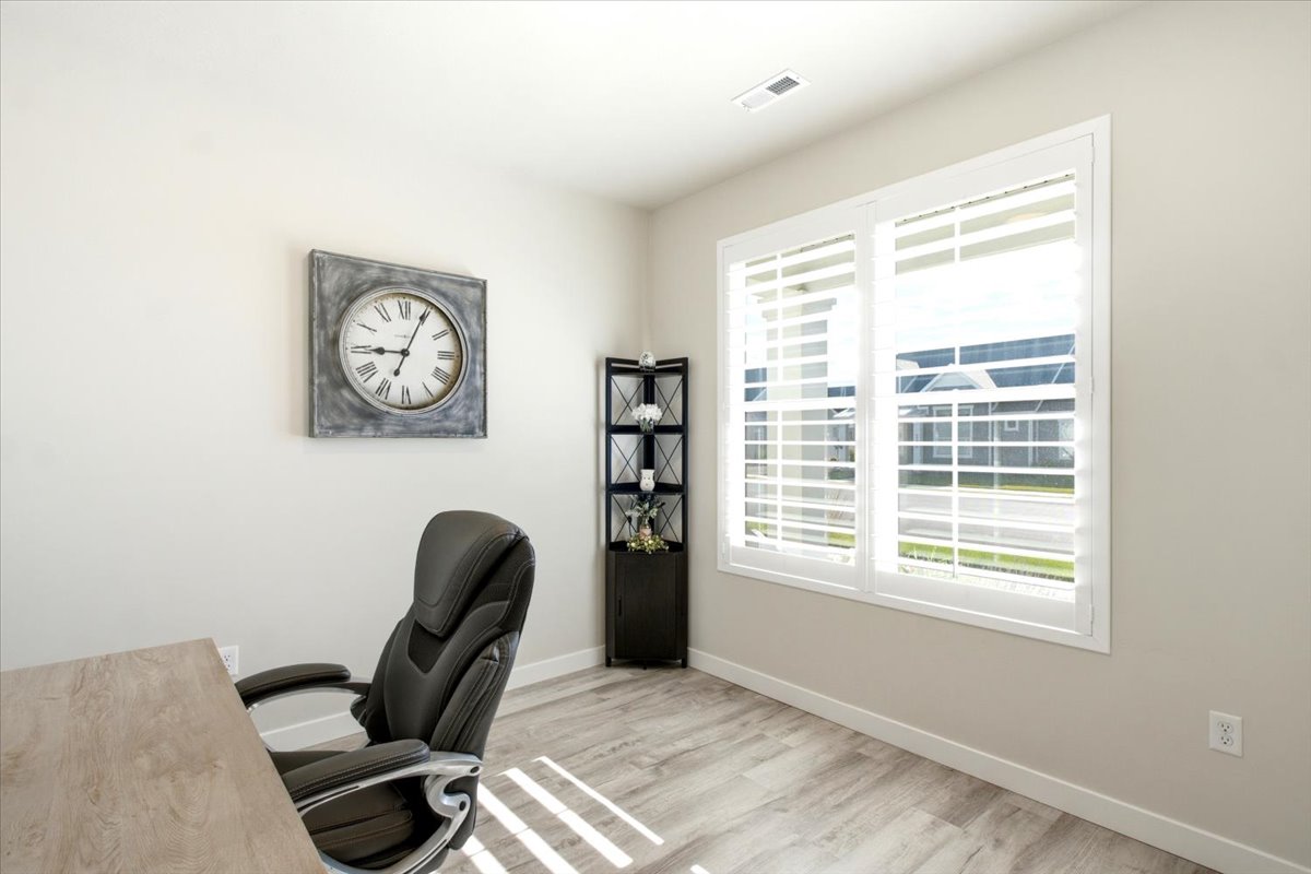 Bright interior space featuring a large window with white plantation shutters, light wood-finish flooring, and neutral wall paint