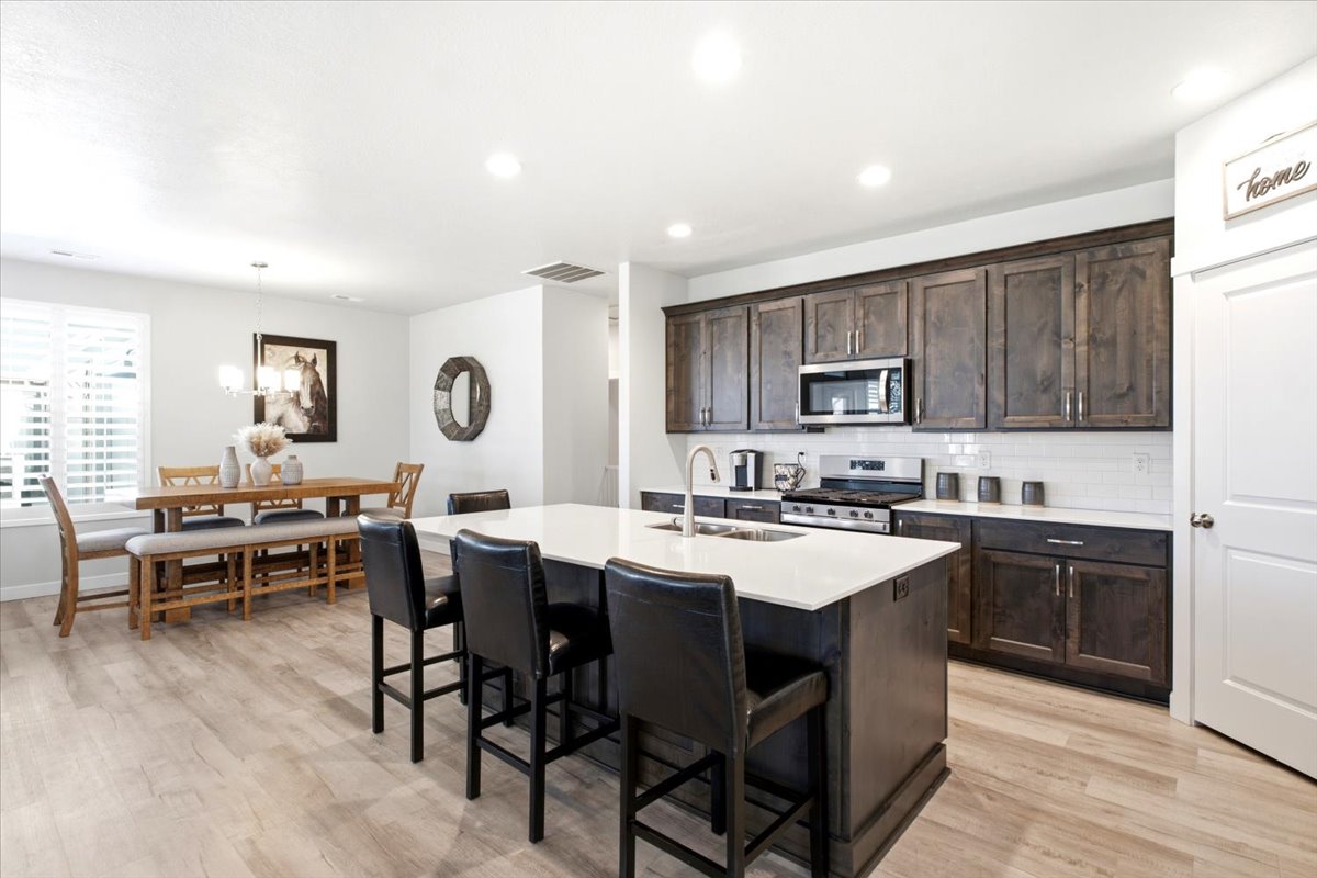 Spacious kitchen featuring an expansive island with seating, stainless steel appliances, dark wood-finish cabinetry, white subway tile backsplash, and wood-finish flooring