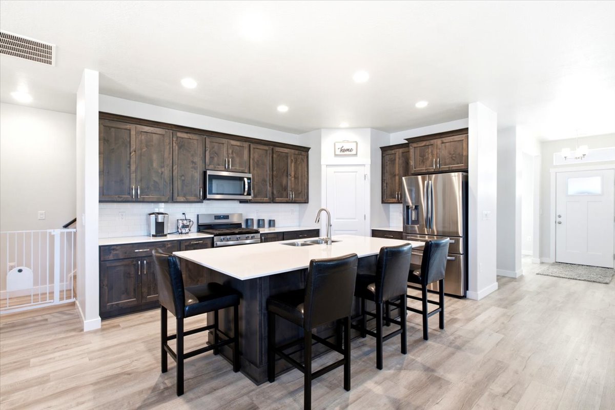 Modern kitchen featuring a central island with seating, dark wood cabinetry, stainless steel appliances, and light-toned wood-finish flooring