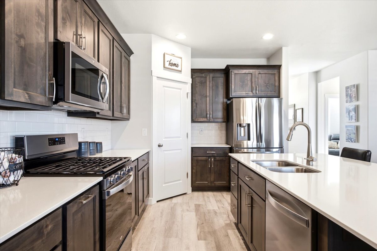 Gourmet kitchen with dark wood cabinetry, stainless steel appliances, white subway tile backsplash, light wood-finish flooring, and a spacious island featuring a double-basin sink