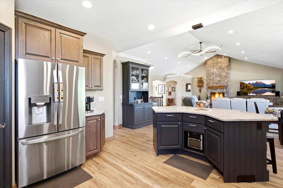 Open-concept kitchen featuring wood-finish flooring, a stainless steel refrigerator, dark cabinetry, and light-toned countertops