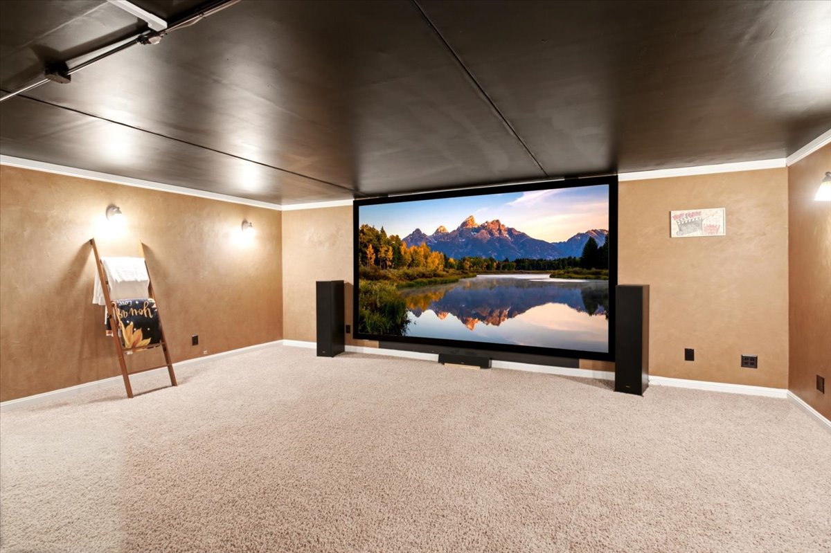 Dedicated entertainment space featuring a large projection screen, wall-mounted sconces, and neutral-toned carpeting