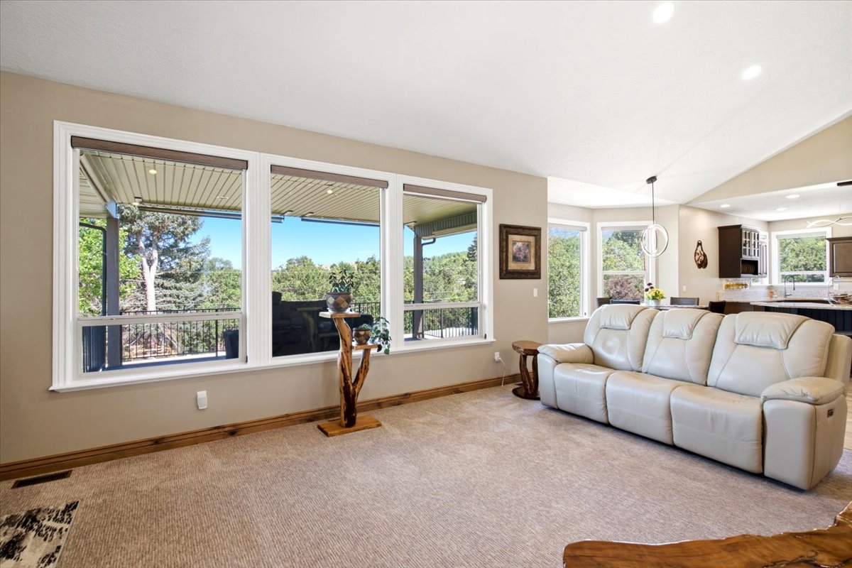 Spacious living area featuring expansive windows, neutral wall tones, vaulted ceilings, and plush carpeting