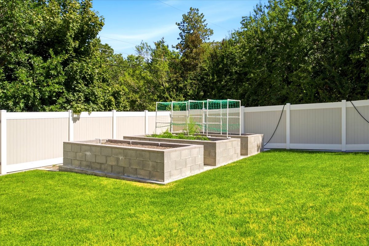 Expansive backyard featuring a lush lawn, three raised garden beds constructed from concrete blocks, and a privacy fence