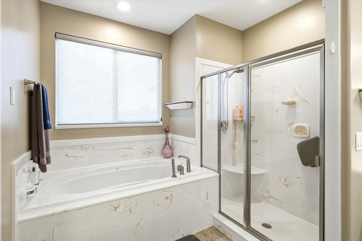Bathroom featuring a built-in soaking tub with a patterned surround, a separate glass-enclosed shower with a built-in bench, and a window with a roller shade