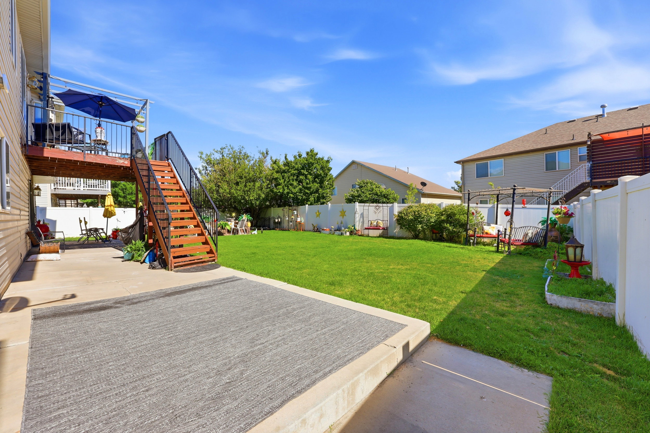 Spacious backyard featuring a substantial lawn, concrete patio, and a raised wood-finish deck with black metal railings
