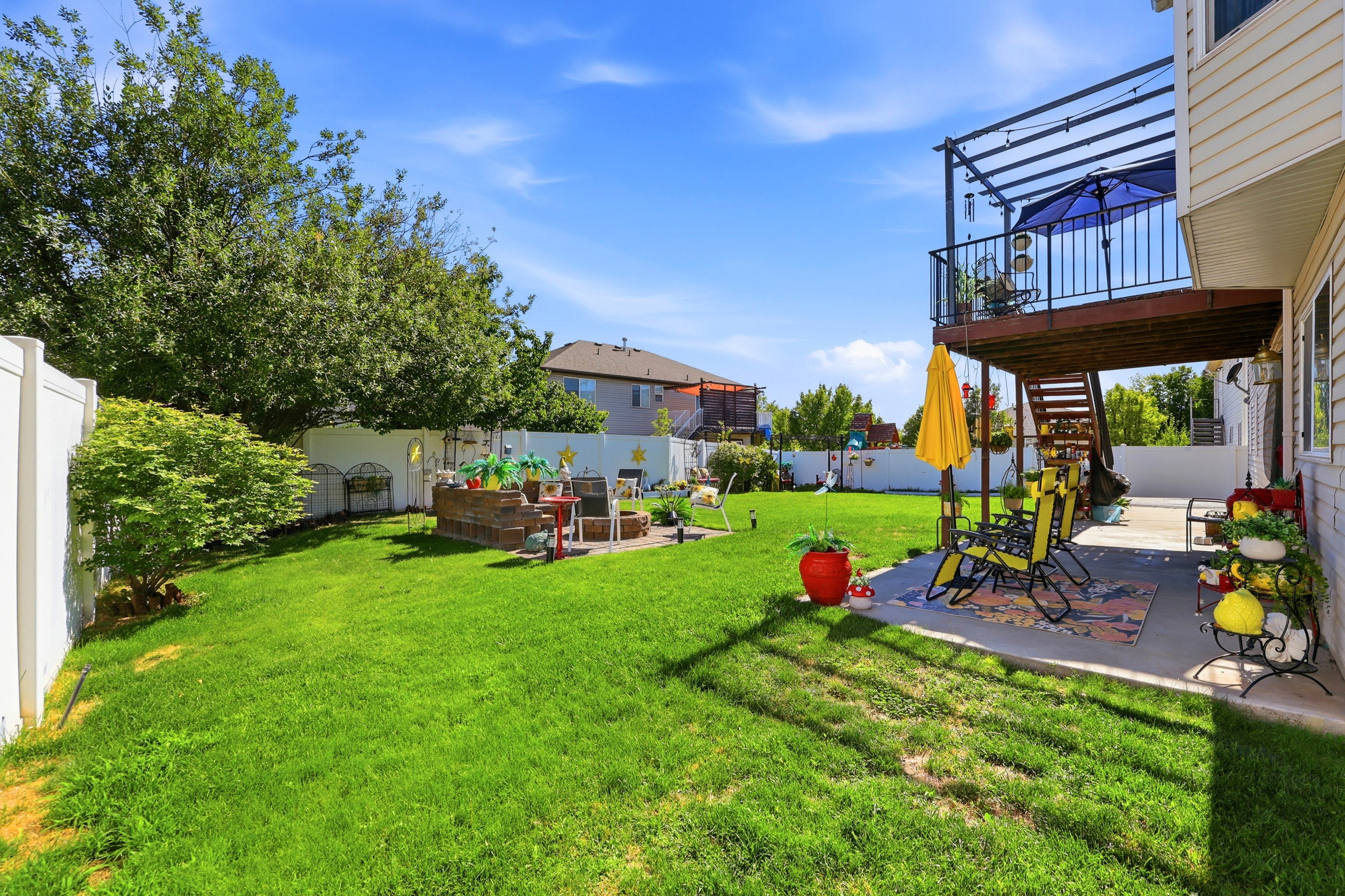Expansive backyard featuring a green lawn, white privacy fencing, a ground-level patio, and a tiered deck with an overhead pergola structure