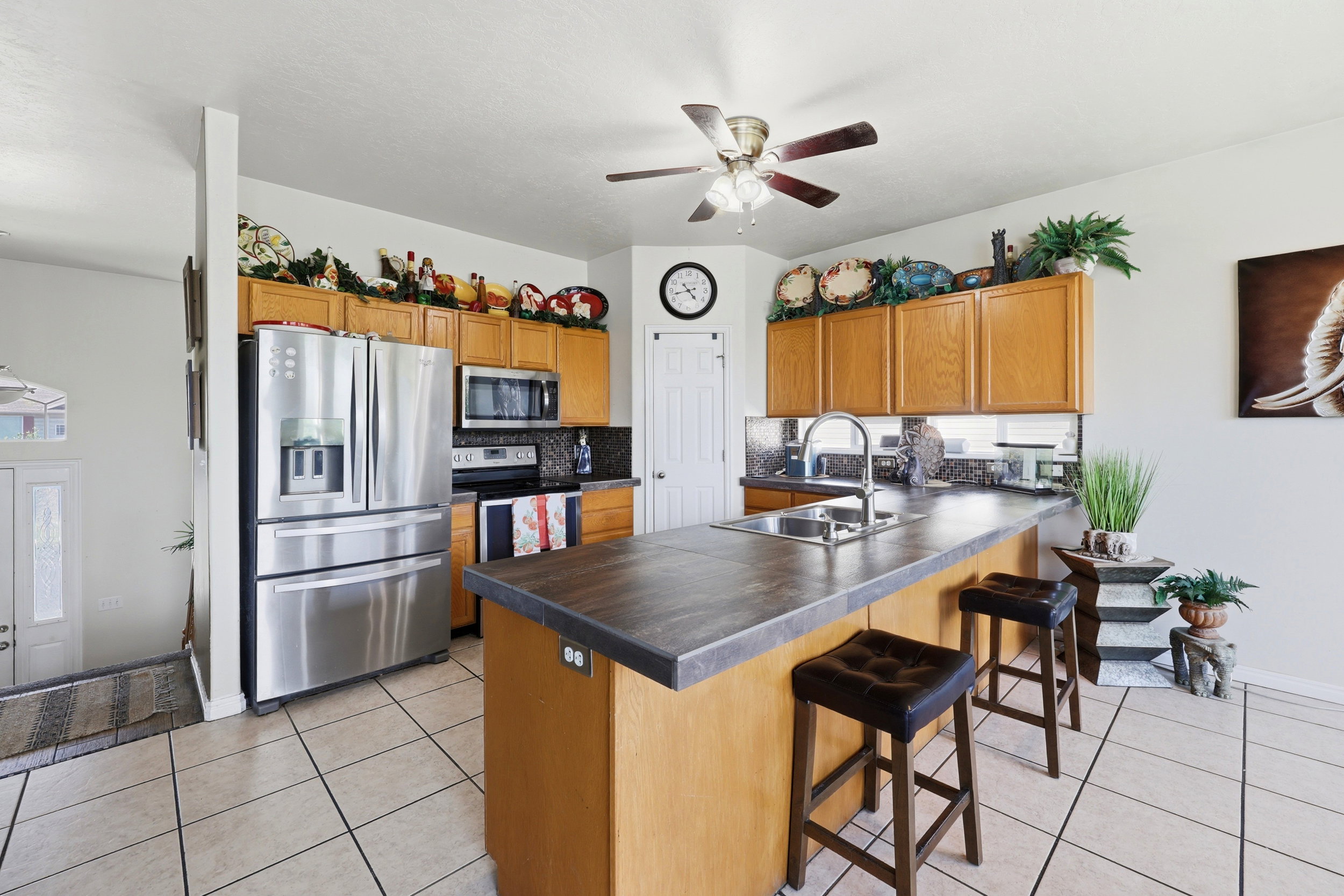 Kitchen featuring an island with integrated sink, stainless steel appliances, wood cabinetry, and tiled flooring