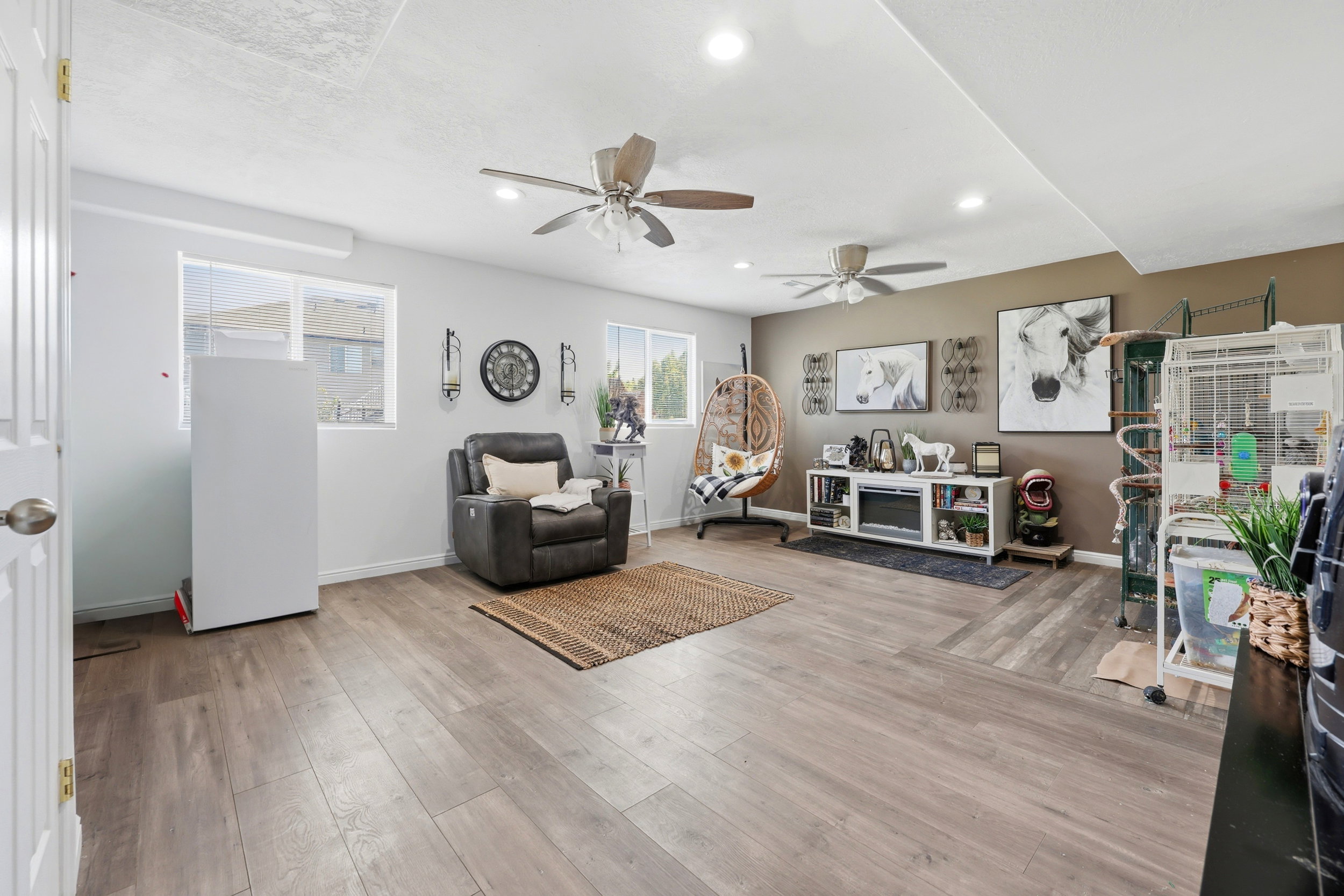 Spacious room featuring wood-finish flooring, two ceiling fans with integrated lighting, recessed overhead lighting, and multiple windows providing natural illumination