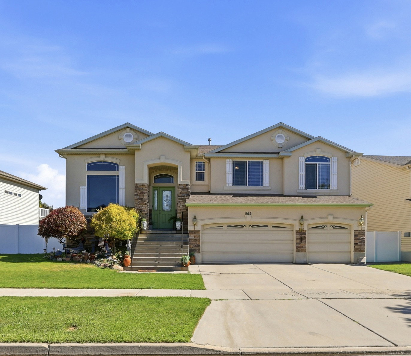 Two-story stucco residence featuring a prominent green entry door, stone accents, arched windows, and a three-car garage