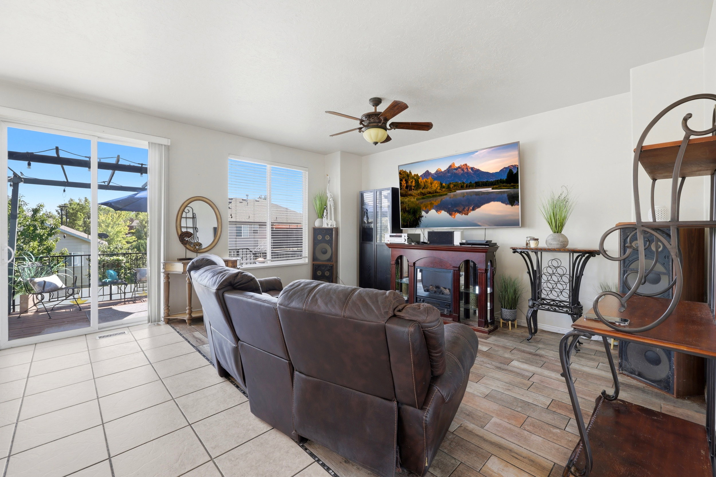 Living area featuring light tile flooring, wood-finish flooring, a ceiling fan, and sliding glass doors opening to an outdoor deck