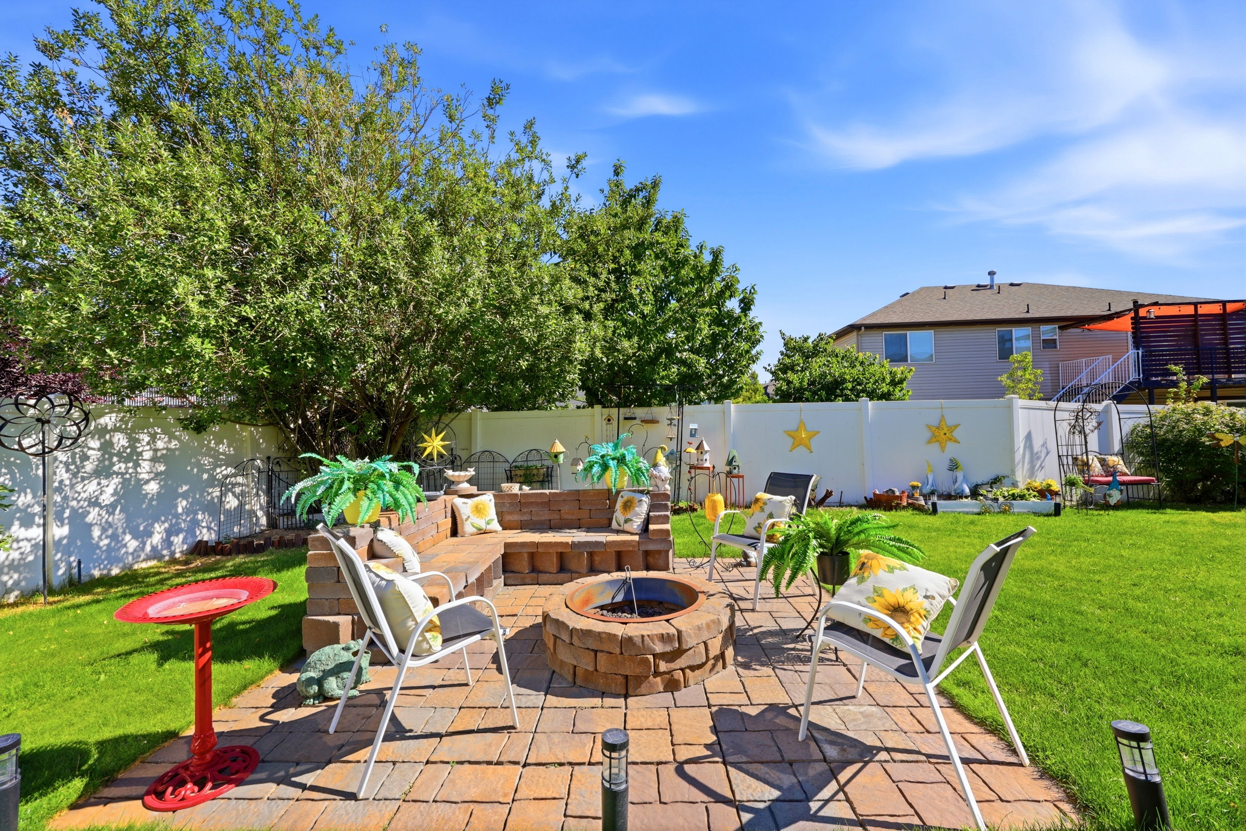 Expansive backyard featuring a paver patio with a built-in fire pit, stone block seating, lush green lawn, and mature trees