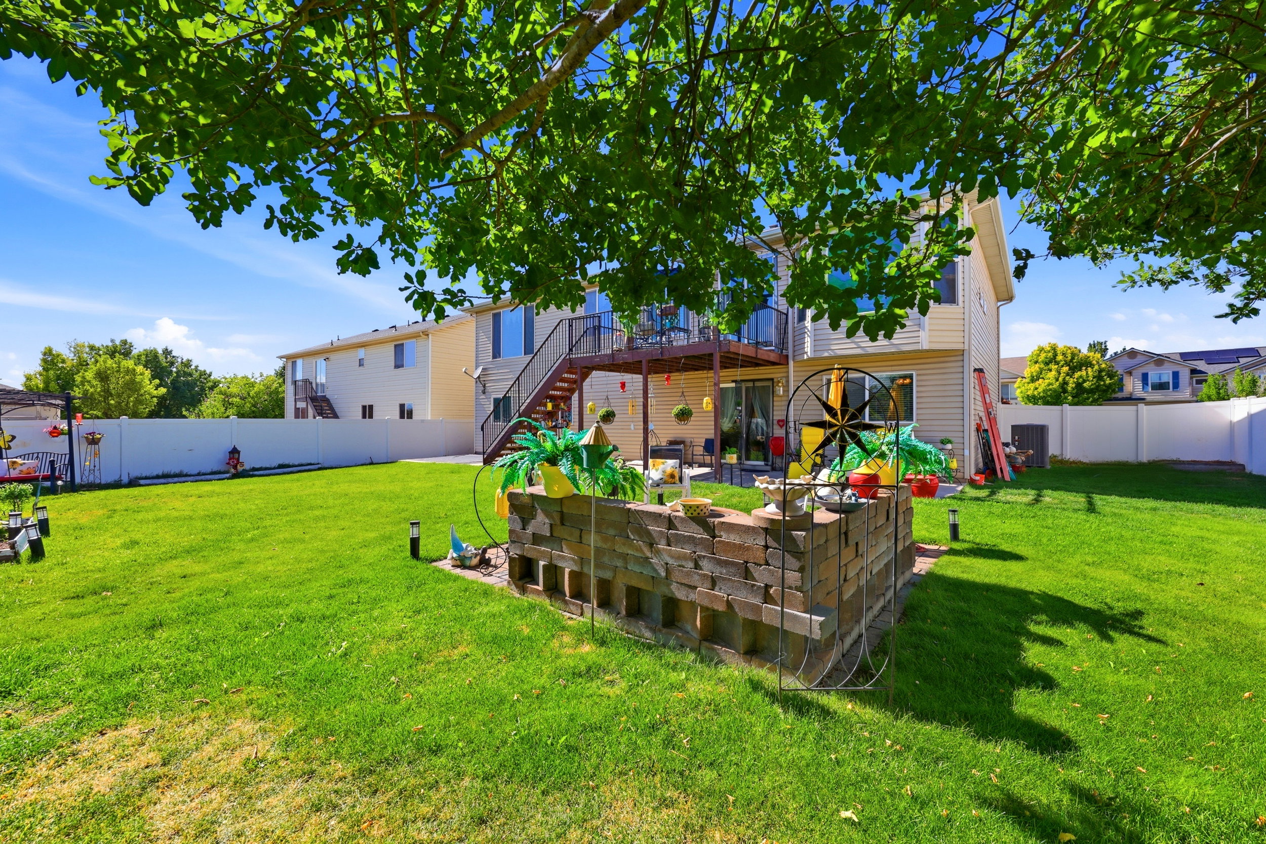 Expansive backyard featuring a lush lawn, privacy fencing, and a two-story residence with an upper-level deck and ground-level patio