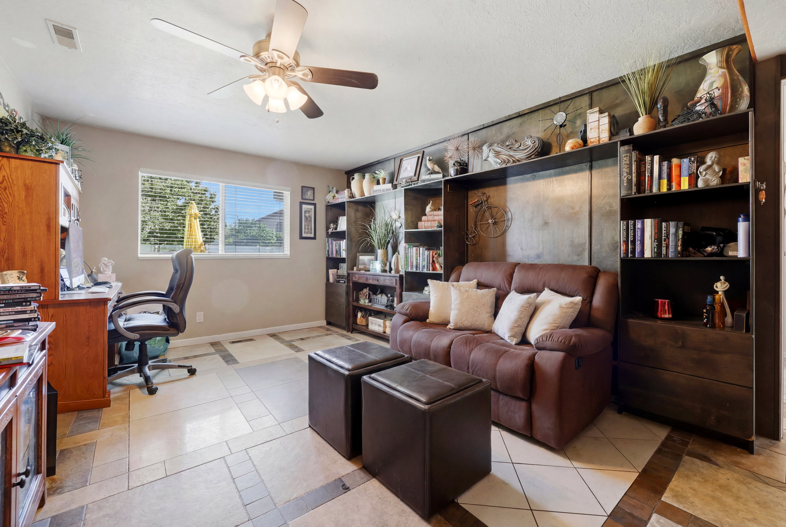 Living area featuring a ceiling fan, a window with blinds, and built-in shelving units