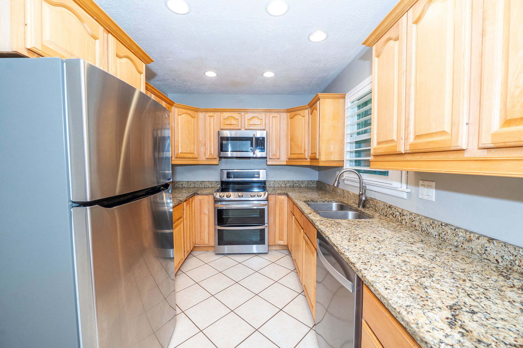 U-shaped kitchen featuring light wood cabinetry, speckled countertops, stainless steel appliances, and a double basin sink