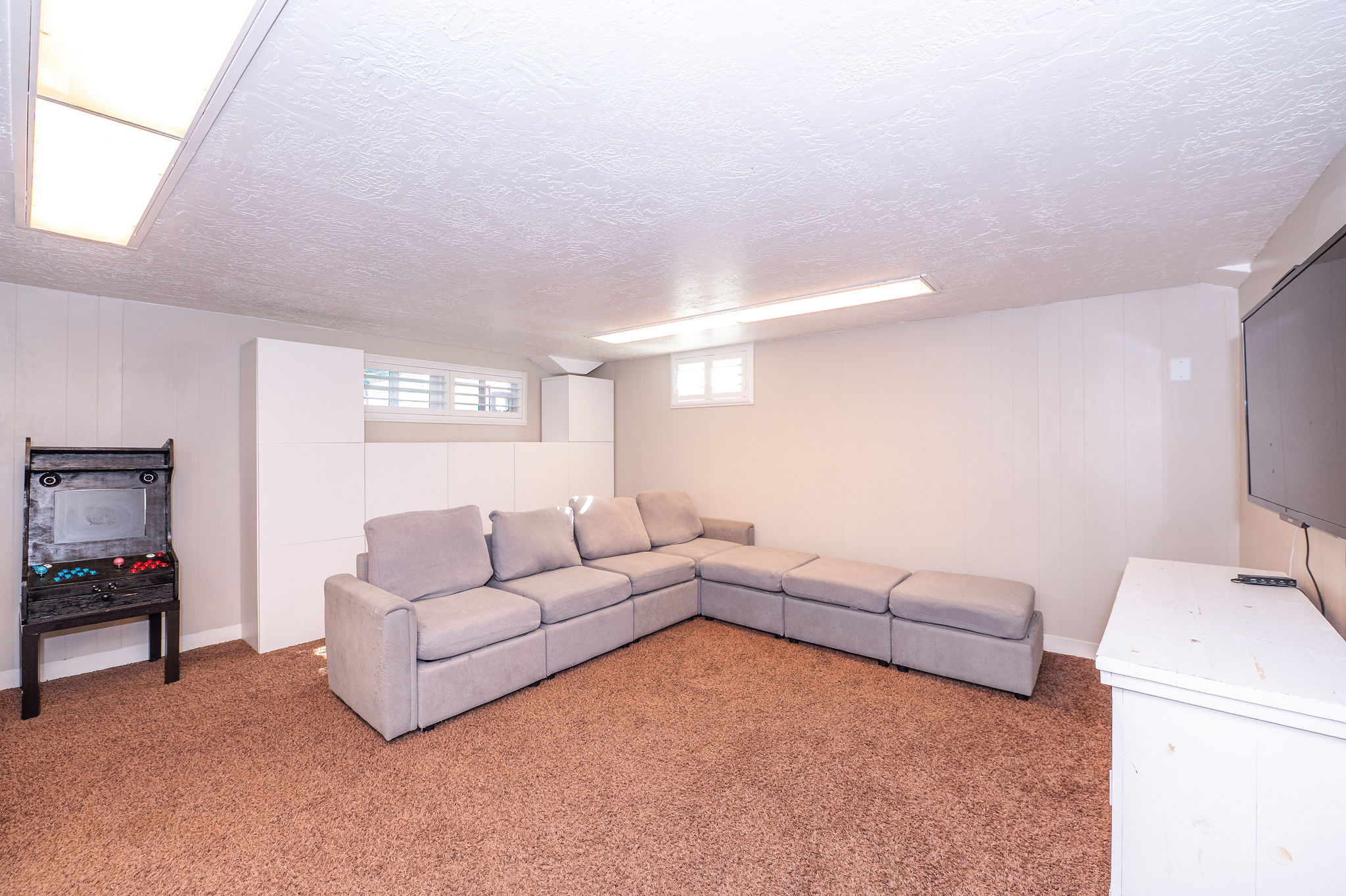 Lower-level room featuring brown carpeting, white walls, and built-in white cabinetry along one wall