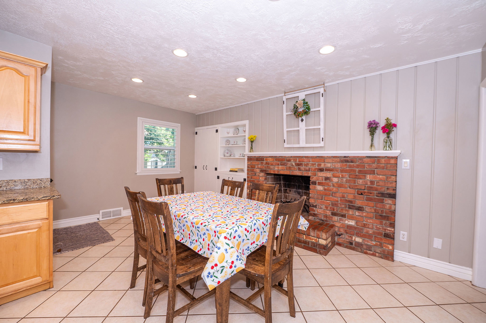 Brick fireplace with a substantial hearth, board and batten accent wall, recessed lighting, tile flooring, and a built-in cabinet with shelving