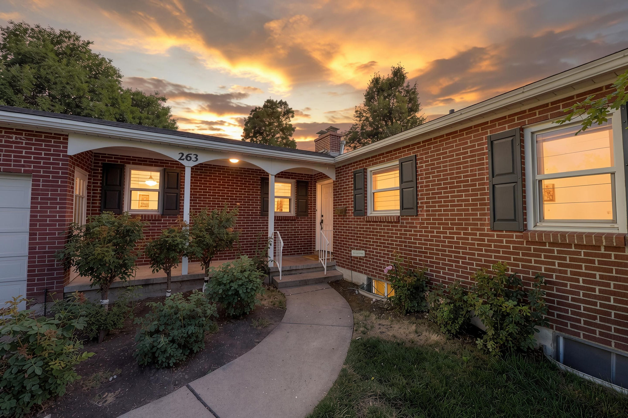 Brick exterior featuring a covered entry porch, dark shutters, and a curved concrete walkway