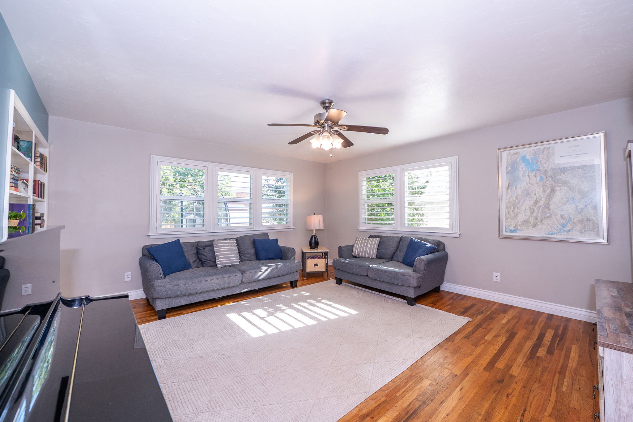 Hardwood flooring throughout a spacious room featuring multiple windows with plantation shutters