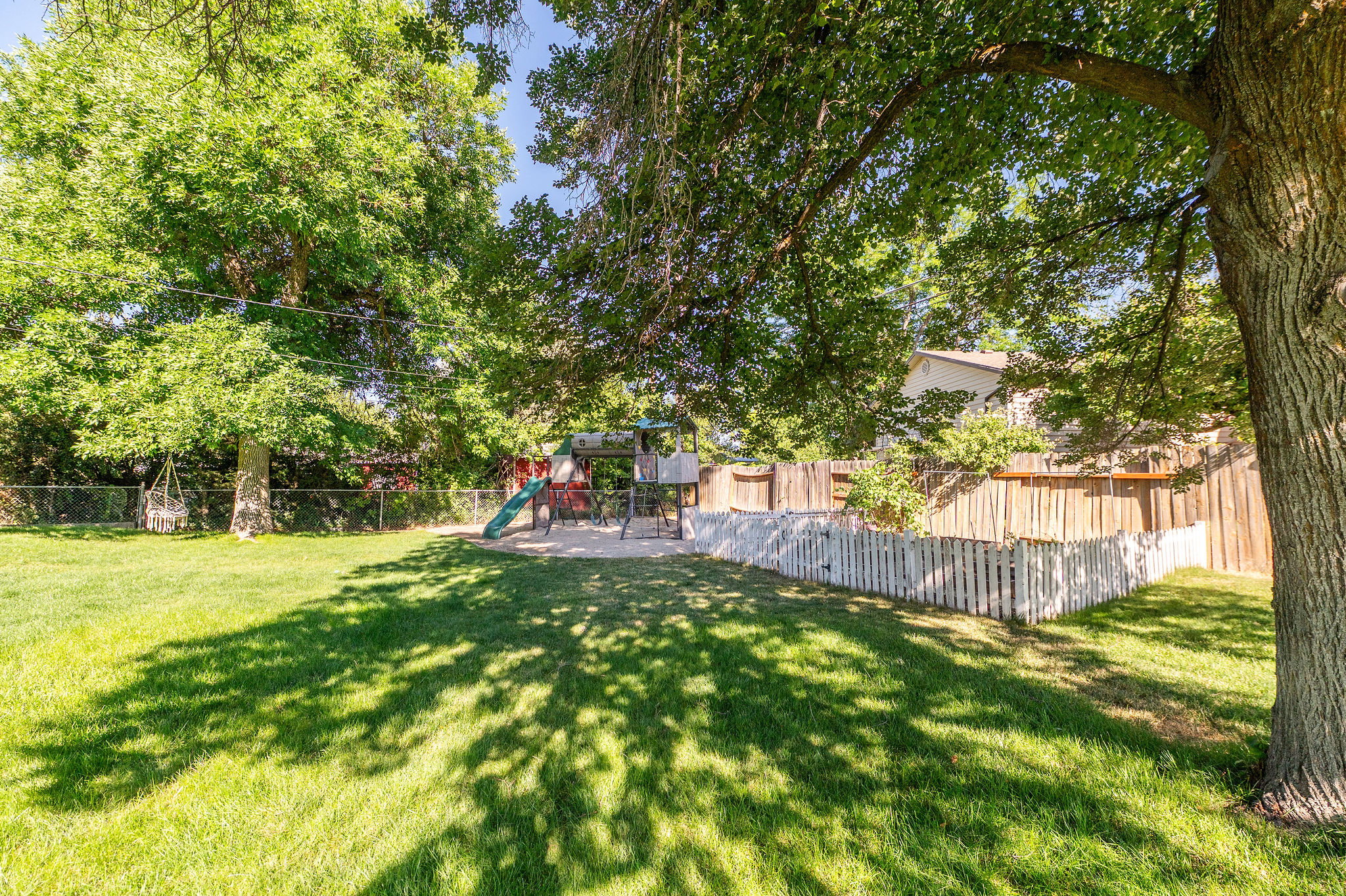 Expansive backyard featuring mature trees, a manicured lawn, and perimeter fencing