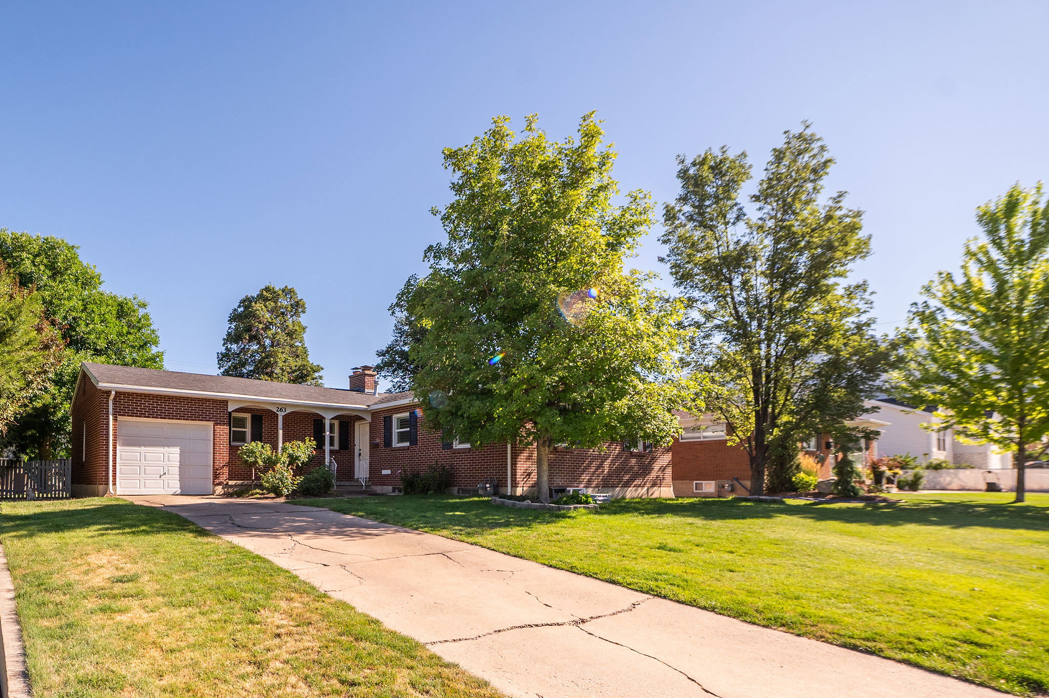 Brick exterior residence featuring a single-car garage, covered porch entry, and mature landscaping