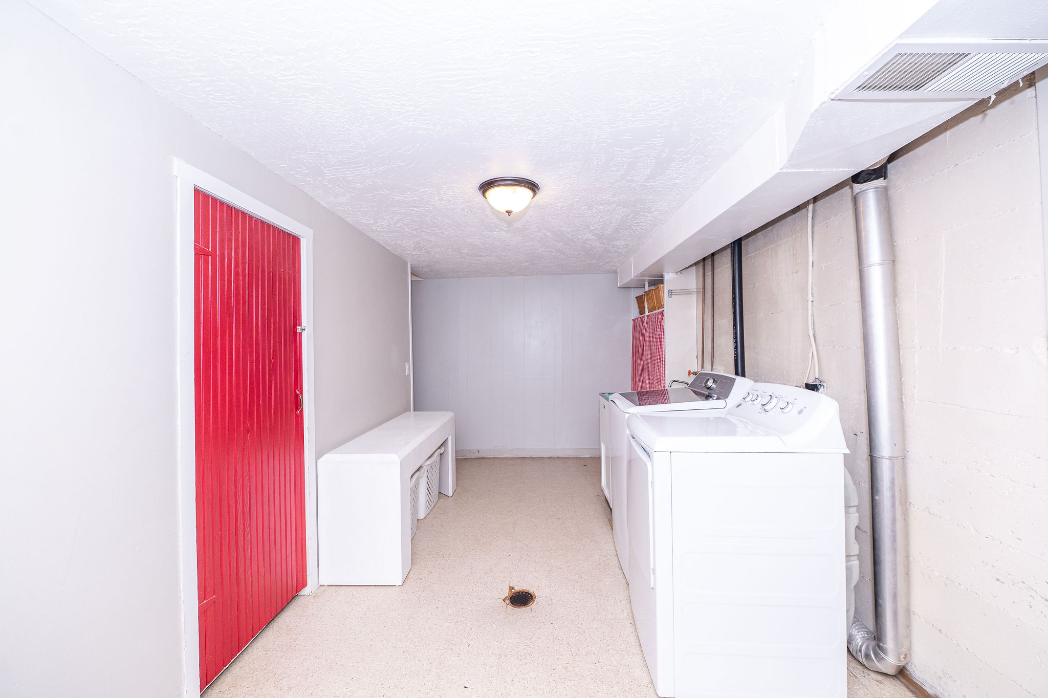 Practical utility space featuring light-colored walls, ceiling-mounted lighting, and a red corrugated door