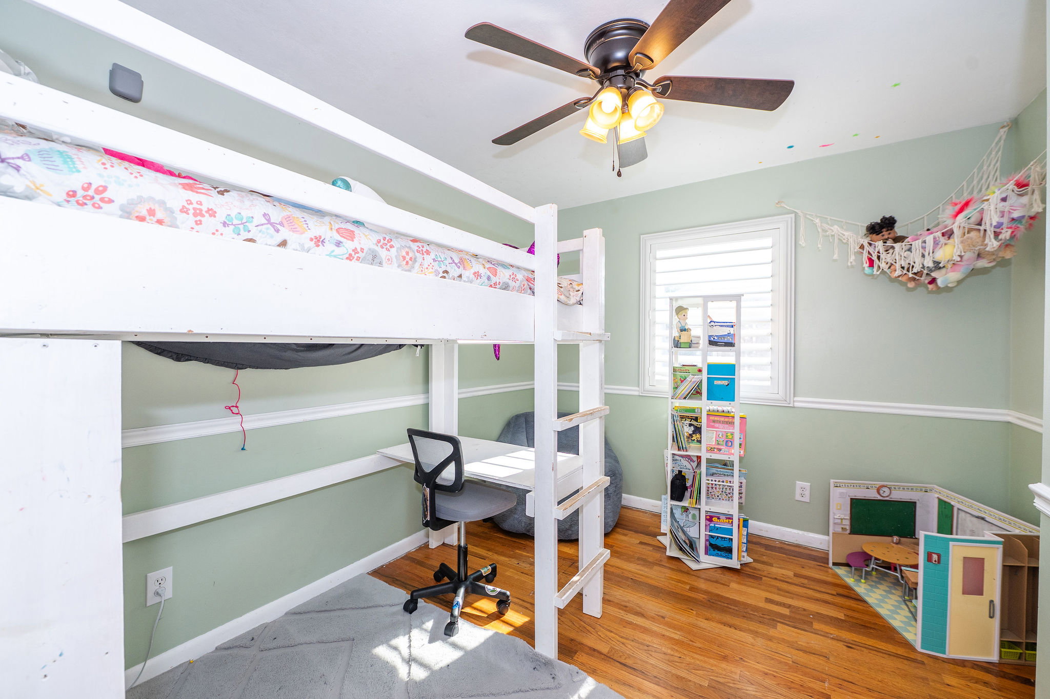 Hardwood flooring throughout featuring a ceiling fan, white window treatments, and two-tone wall paint with wainscoting