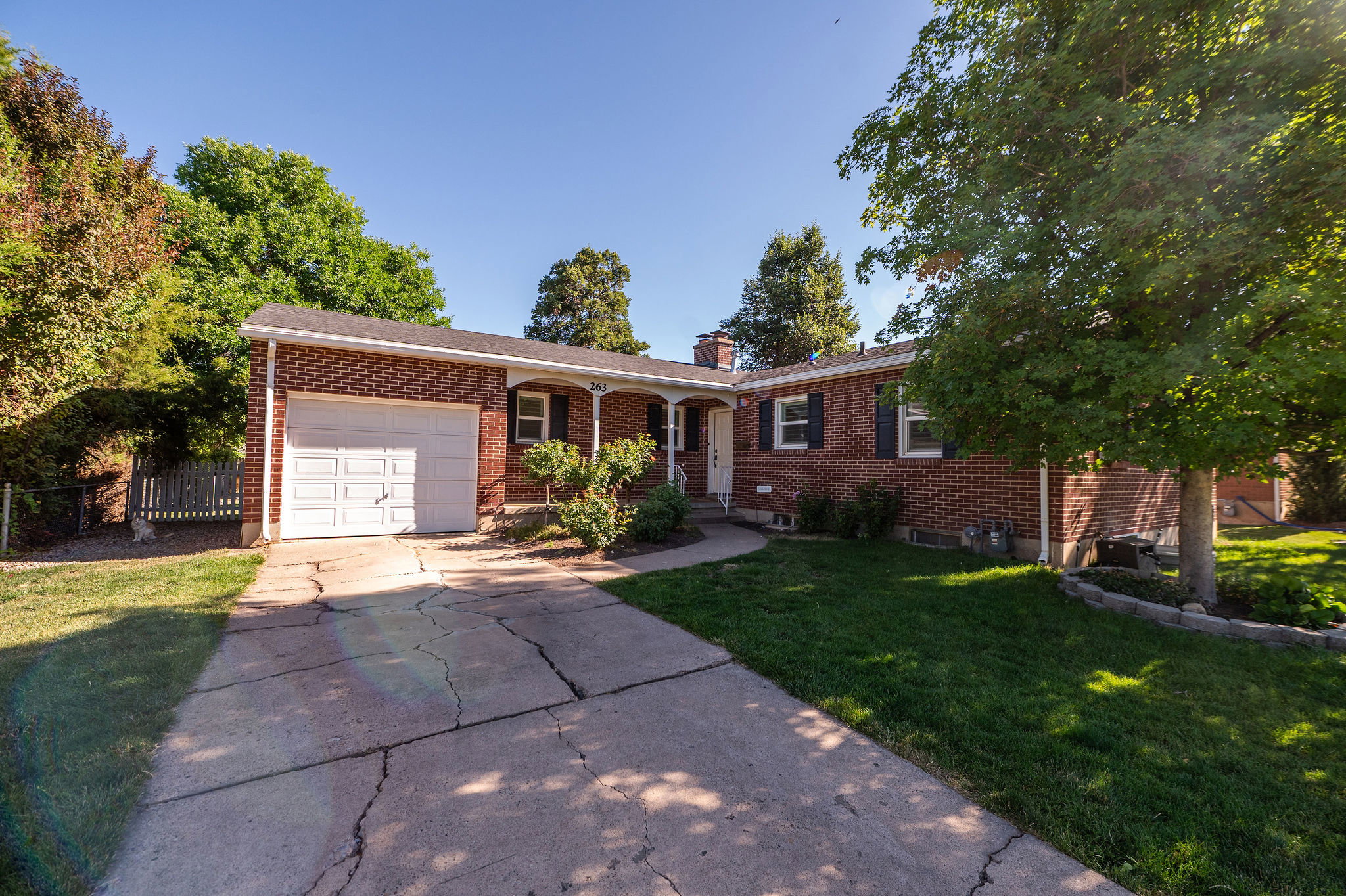 Brick exterior featuring a covered porch entry, attached garage with a white door, established landscaping, and a concrete driveway