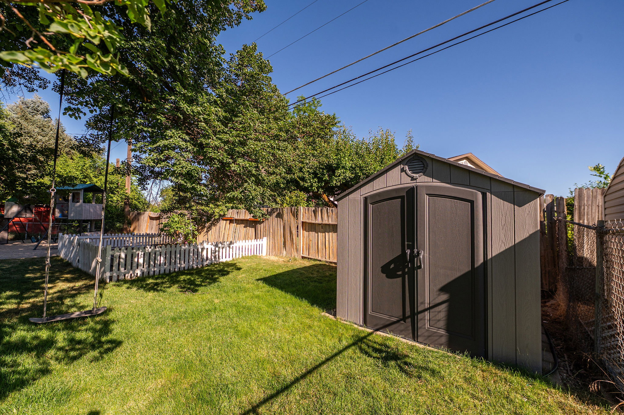 Private backyard featuring a freestanding storage shed, a white picket fence, and mature trees providing natural shade