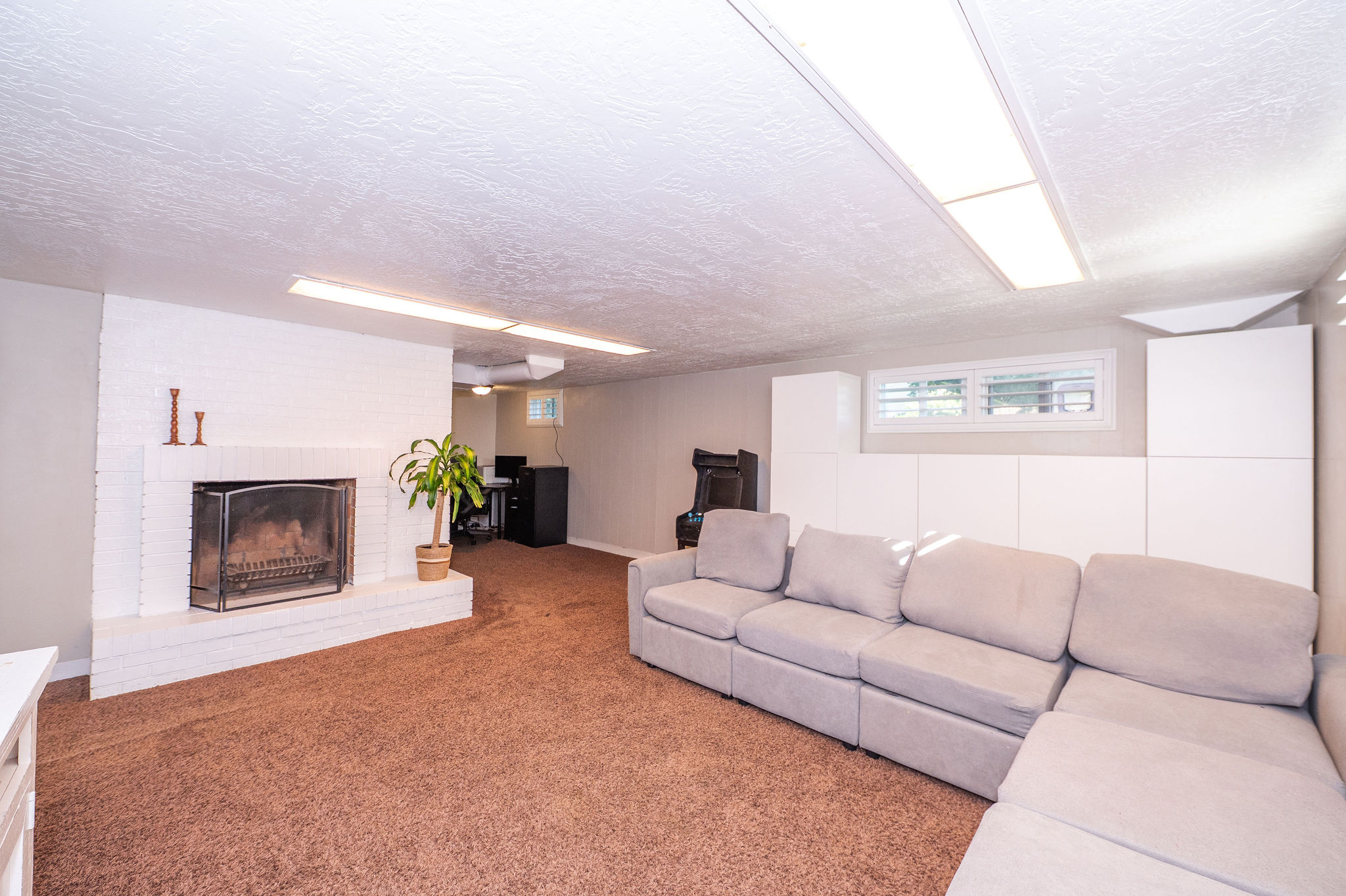 Finished basement space featuring a white brick fireplace, recessed lighting, and built-in white cabinetry