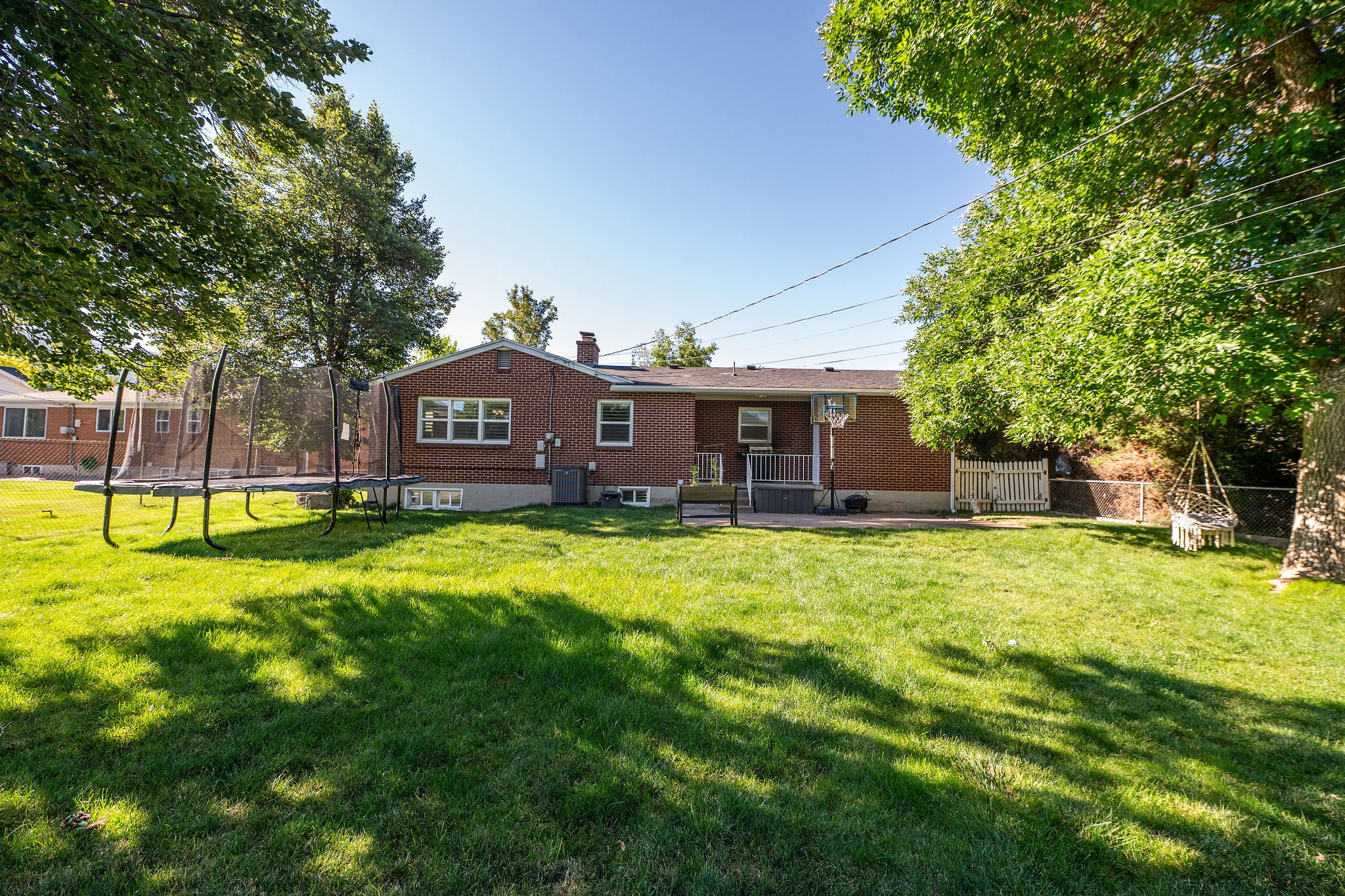 Expansive backyard featuring a manicured lawn, mature trees providing shade, and a brick exterior home with multiple windows