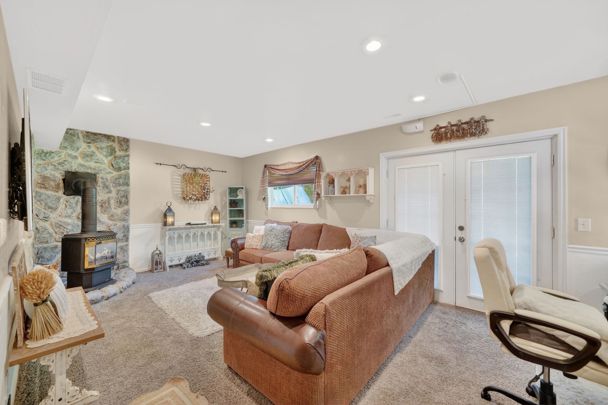 Recessed lighting illuminates a carpeted living space featuring a stone-clad wall with a wood-burning stove on a stone hearth