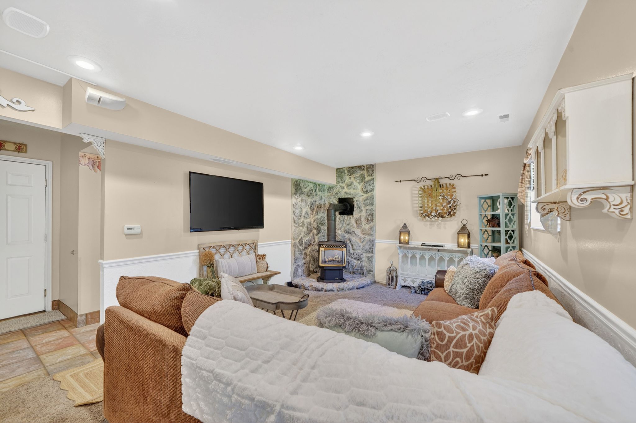 Living area featuring a stone accent wall, a wood-burning stove with a metal flue, recessed lighting, and a white paneled wainscoting