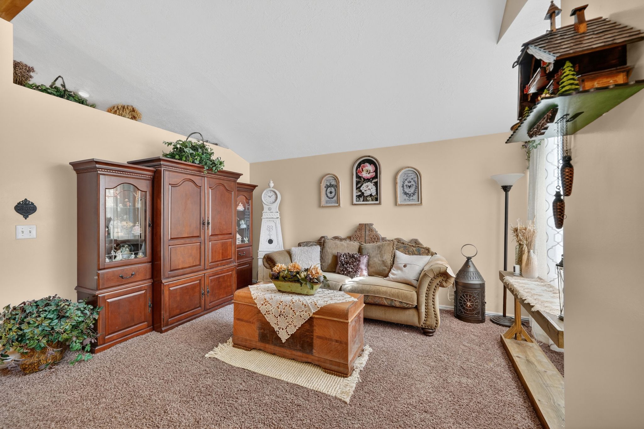 Vaulted ceiling interior featuring a built-in wall unit with glass display cabinetry, a carpeted floor, and a decorative wall niche