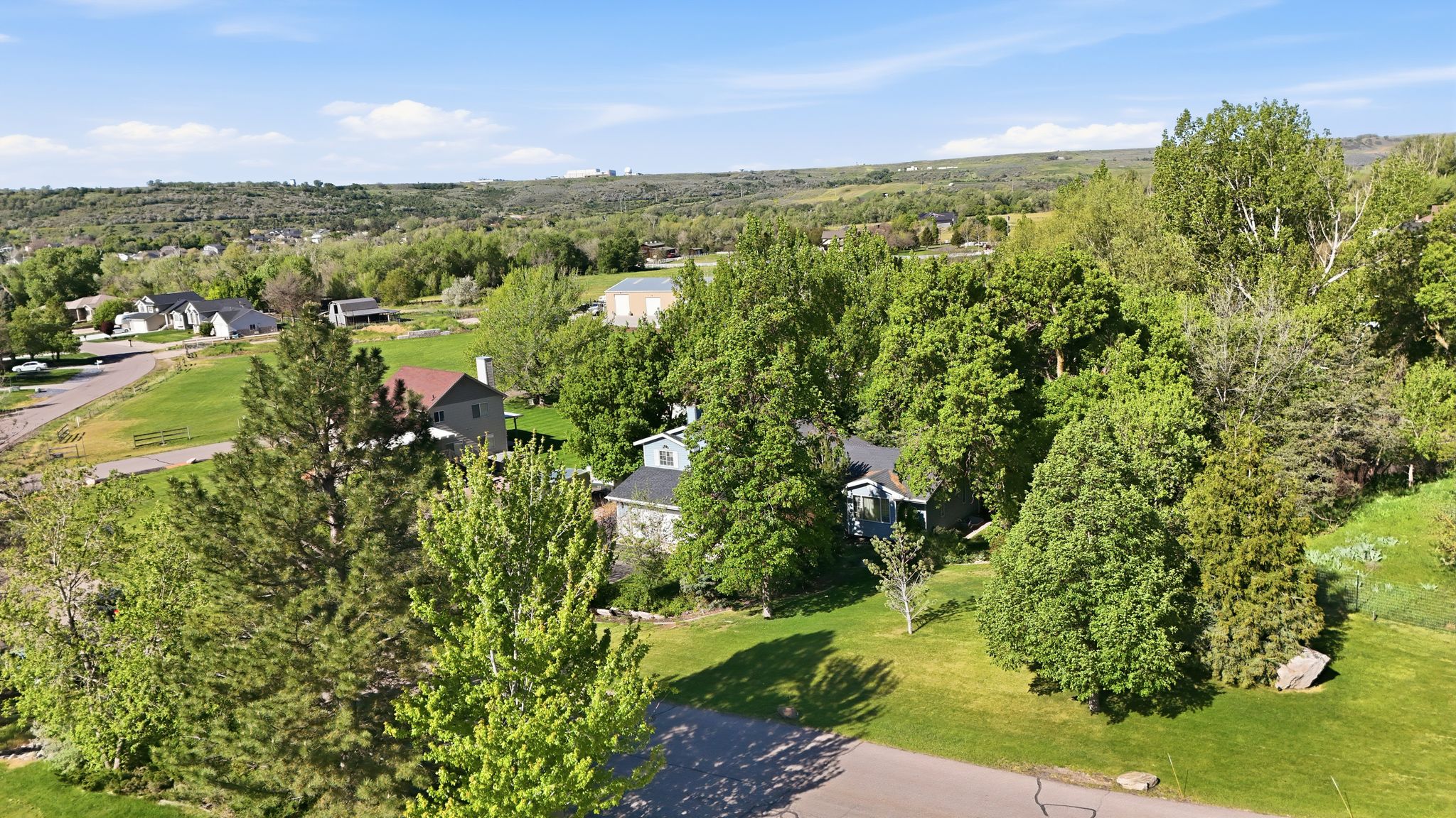 Expansive residential landscape featuring mature trees, green lawns, and a clear blue sky