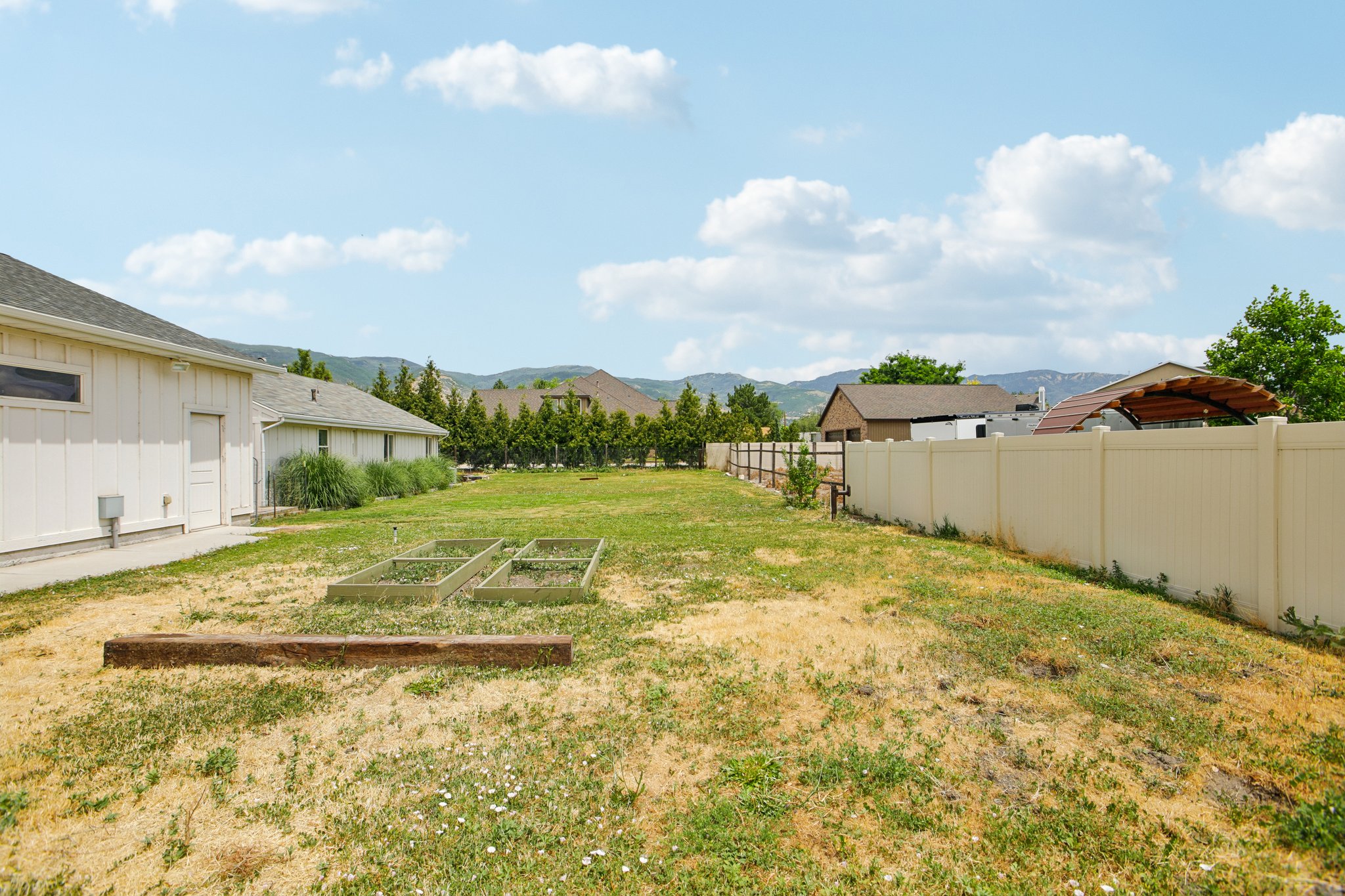 Expansive backyard with a level lawn area, raised garden beds, and a perimeter fence